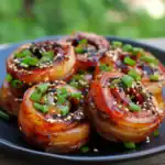 Sweet and savory bacon-wrapped scallops topped with chopped green onions and sesame seeds, served on a dark plate, showcasing a delicious seafood appetizer perfect for special occasions.