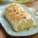 Cream cheese roll with shredded cheese, chopped nuts, and pistachio toppings on a decorative blue platter, perfect for appetizer or party tray.