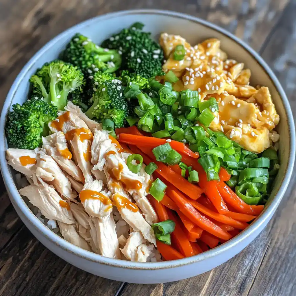 Fresh healthy chicken and vegetable rice bowl with broccoli, carrots, scrambled eggs, green onions, and teriyaki sauce, ideal for quick meals and nutritious eating.