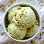 Creamy pistachio ice cream with chopped pistachio toppings in a white bowl, perfect for summer desserts.
