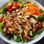 Grilled chicken salad with fresh vegetables, cherry tomatoes, shredded carrots, and slivered almonds, drizzled with a savory dressing. Perfect for healthy and delicious lunch or dinner.