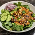 Grilled chicken salad with fresh cucumbers, red onions, cilantro, and chopped peanuts on a white plate, featuring vibrant, healthy ingredients perfect for a nutritious meal.