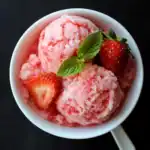 Fresh strawberry sorbet with mint leaves and sliced strawberries in a white bowl, perfect for summer desserts.