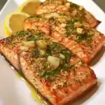 Salmon fillets with garlic, herbs, and lemon slices on a white plate, seasoned and cooked to perfection. An easy and healthy seafood recipe perfect for quick dinners or special occasions.