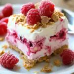 Fresh raspberry icebox cake with graham cracker crust, whipped cream, and crushed cookies, topped with fresh raspberries for a delicious summer dessert.