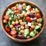 Fresh chickpea salad with cucumbers, cherry tomatoes, red onions, kalamata olives, feta cheese, and herbs in a wooden bowl for healthy eating.