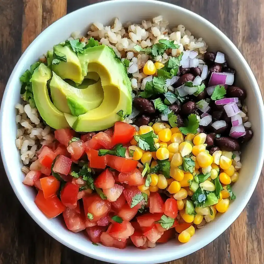 Fresh veggie burrito bowl with avocado, black beans, corn, tomatoes, onions, and cilantro on brown wooden surface.