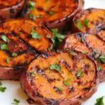 Grilled sweet potatoes topped with fresh herbs and BBQ sauce, served on a white platter for a healthy and flavorful side dish or appetizer. Perfect for summer barbecues and meal prep.
