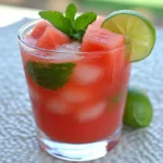 Watermelon lemonade refresher with fresh mint and lime slices on a textured surface perfect for hot summer days.
