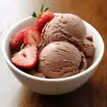 Creamy chocolate ice cream with fresh strawberries in a white bowl. Perfect homemade dessert for summer or special occasions. Served chilled for a sweet and indulgent treat.