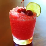 Refreshing cherry limeade cocktail with crushed ice, topped with fresh cherries and lime wedge, perfect for summer beverages and cocktail recipes.
