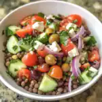 Fresh lentil salad with tomatoes, cucumbers, red onions, kalamata olives, feta cheese, and fresh parsley in a white bowl, perfect for healthy meal options.