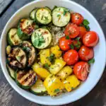 Fresh grilled zucchini, cherry tomatoes, yellow bell peppers, and quinoa bowl in a white dish, garnished with chopped herbs, healthy vegetable meal, vegan-friendly, colorful, nutritious, and delicious.
