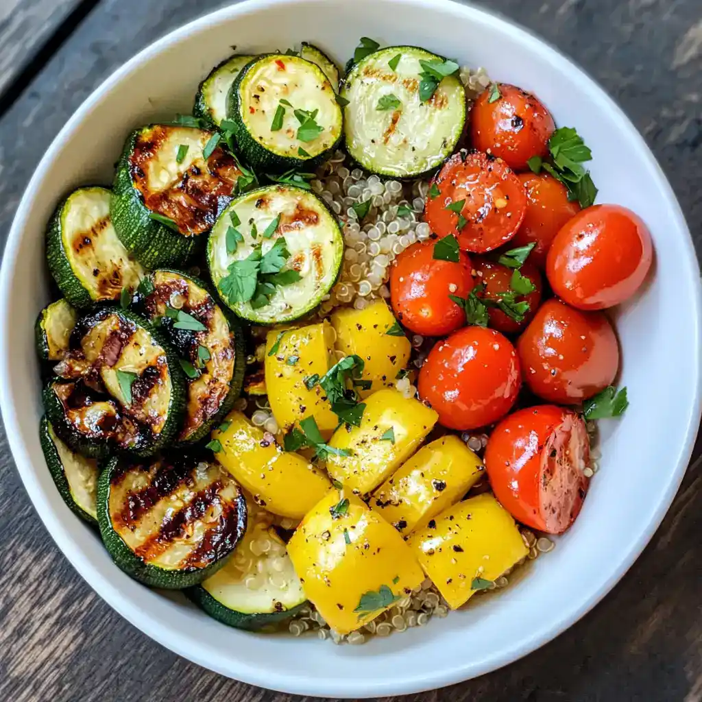 Fresh grilled zucchini, cherry tomatoes, yellow bell peppers, and quinoa bowl in a white dish, garnished with chopped herbs, healthy vegetable meal, vegan-friendly, colorful, nutritious, and delicious.