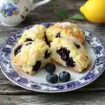 Fresh blueberry scones served on a vintage blue and white plate with fresh blueberries and a lemon in the background. Perfect for breakfast or brunch, featuring homemade, flaky, and fruity flavors.