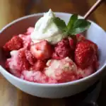 Fresh strawberry sorbet with whipped cream and mint garnish in a white bowl, showcasing a fruity and refreshing dessert perfect for summer.