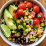Fresh quinoa salad with cherry tomatoes, avocado, corn, black beans, cucumber, cilantro, red onion, and lime wedge, perfect for healthy eating, vegan recipes, and summer meals.