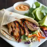 Grilled chicken fajita wrap with fresh salad and lime wedges on white plate, high-quality close-up, healthy Mexican-inspired dinner option.