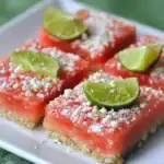 Fresh watermelon bars topped with lime wedges and coconut flakes on white plate, a delicious summer fruit dessert from Station Recipes.