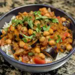 Creamy Chickpea and Eggplant Curry over White Rice, garnished with fresh cilantro, served in a black bowl. A hearty, flavorful vegetarian dish perfect for lunch or dinner, packed with spices and wholesome ingredients.