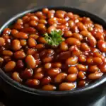 Sweet baked beans in a black bowl garnished with a sprig of parsley, perfect for classic comfort food recipes.