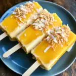 Creamy mango popsicles with coconut topping, perfect for summer treats and refreshing dessert recipes. Vibrant yellow color; ideal for family-friendly frozen treats.