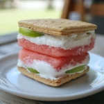 Fresh watermelon ice cream sandwich with graham crackers, cream cheese, and lime on a white plate, perfect for summer desserts.