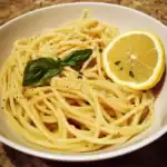Lemon spaghetti with fresh basil and black pepper in a white bowl, featuring a lemon slice garnish, fresh herbs, and a creamy lemon sauce. Delicious, easy pasta recipe perfect for quick dinners.