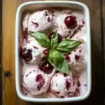 Creamy cherry ice cream with fresh cherries and a basil garnish in a white ramekin - perfect homemade dessert.