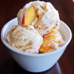 Sweet peach and vanilla ice cream with fresh peach slices in a white bowl, perfect for summer desserts.