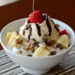 Sweet dessert bowl with fresh strawberries, bananas, chocolate chips, chopped nuts, whipped cream, and chocolate syrup. Perfect for a tasty treat or breakfast.