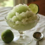 Refreshing lime granita dessert served in a glass bowl with lime slices for garnish. Perfect for summer, made with fresh lime juice, sugar, and ice for a cooling treat from Station Recipes.
