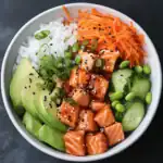 Fresh salmon poke bowl with avocado, cucumber, shredded carrots, rice, green onion, and sesame seeds, perfect for healthy eating and sushi-style meals.