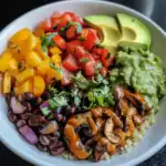 Fresh vegan burrito bowl with black beans, quinoa, avocado, pico de gallo, roasted peppers, and guacamole on a white plate, healthy plant-based meal, colorful and nutritious vegetarian dish.