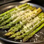 Fresh roasted asparagus spears topped with grated Parmesan cheese, seasoned with black pepper on a skillet. Perfect side dish for any meal, easy to prepare and full of flavor.