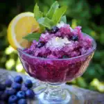 Fresh blueberry and mint granita with lemon wedge in glass bowl, summer fruit dessert, homemade frozen blueberry treat, vibrant and refreshing berry sorbet, perfect for hot days.