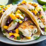 Grilled fish tacos with mango salsa, cabbage slaw, and fresh cilantro on soft tortillas, served on a plate. Perfect for a flavorful, healthy Mexican-inspired meal at home.