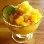 Refreshing frozen lemon and mango snow dessert in a glass bowl for summer cooling, topped with lime wedge, served as a sweet treat on hot days, perfect healthy snack.