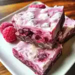 Fresh raspberry fudge squares with a creamy berry swirl, topped with powdered sugar, served on a white dish. Perfect for raspberry dessert recipes and homemade sweet treats.