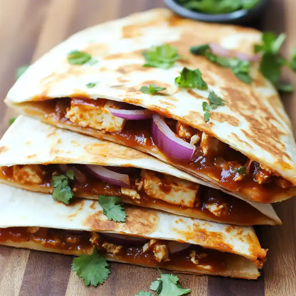 Savory chicken quesadillas filled with melted cheese, beans, and spicy sauce, garnished with fresh cilantro and red onions on a rustic wooden table. Perfect for quick, tasty meals or snacks.