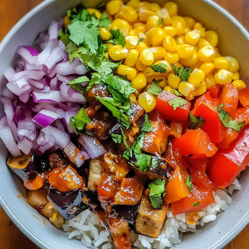 Colorful vegetarian bowl with diced red onions, corn, roasted eggplant, chopped tomatoes, fresh cilantro, and white rice - healthy and vibrant meal idea.