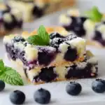 Sweet blueberry cheesecake bars topped with fresh mint leaves, featuring a buttery crust and creamy cheese filling with ripe blueberries. Perfect for dessert or snack enjoyments.