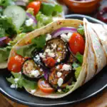 Roasted eggplant and vegetable wrap with feta cheese, fresh greens, cherry tomatoes, and red onions on a soft tortilla for a healthy meal.