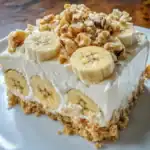 Banana cream cake topped with chopped nuts, fresh banana slices, and creamy frosting, featuring a graham cracker crust, perfect for homemade dessert recipes.