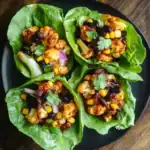 Buffalo Cauliflower Lettuce Wraps with Black Beans, Corn, Red Onion, and Cilantro – healthy vegan appetizer, easy to make, perfect for parties or snacks. Fresh lettuce cups filled with spicy cauliflower and vegetable toppings.