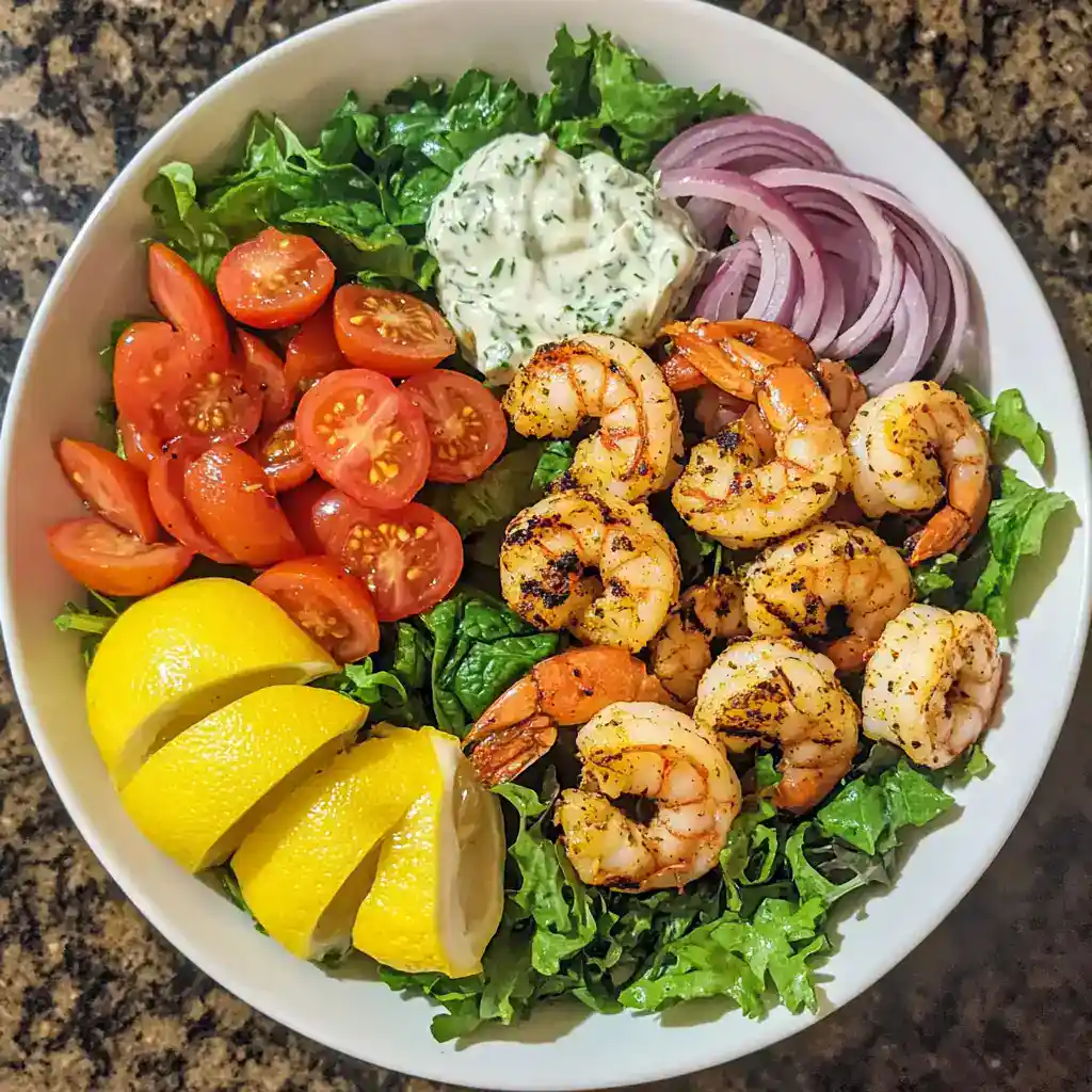 Grilled shrimp salad with cherry tomatoes, red onions, cucumber, lemon wedges, and a dollop of herb dressing. Fresh, flavorful seafood salad perfect for healthy eating.