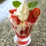 Fresh strawberry shortcake parfait with whipped cream and mint garnish in a glass.