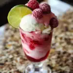 Fresh berry parfait with frozen raspberries, lime wedge, and creamy ice cream, served in a tall glass, perfect for summer desserts.