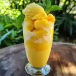 Smooth mango sorbet in a tall glass garnished with fresh mint leaves for a refreshing tropical dessert.