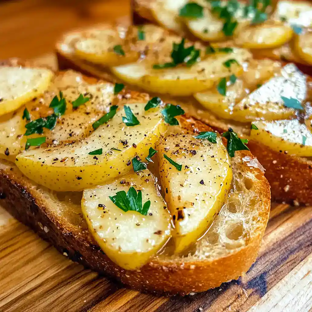 Thinly sliced baked potatoes on toasted bread garnished with herbs, black pepper, and olive oil, making a delicious and flavorful potato toast recipe.